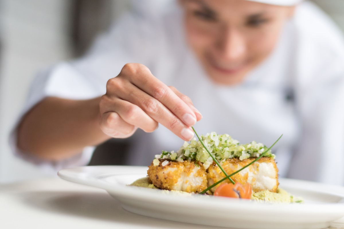 Cook decorating a plate and putting the ultimate touches - focus on foreground